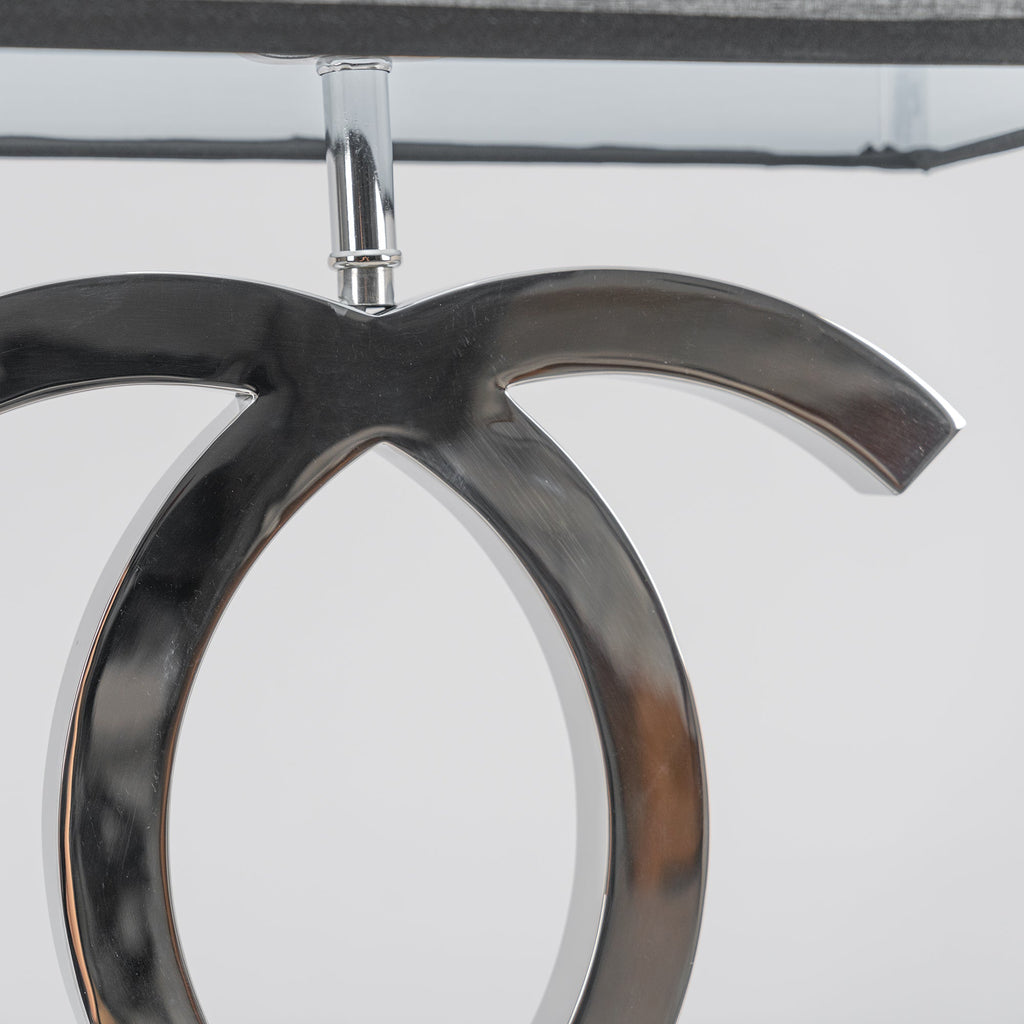 Close view of the polished stainless steel loops below the shade stem on this Clérachic table lamp, against a pale backdrop.