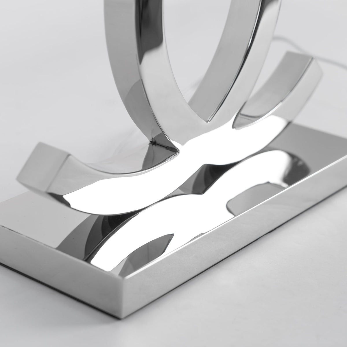 Close view of the mirror-polished steel base and the lower ends of the loops on this Clérachic table lamp.