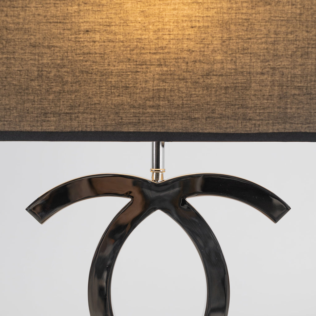 Close view of the textured black fabric shade glowing amber above the dark chrome loops of this Clérachic table lamp.