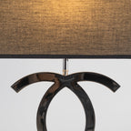 Close view of the textured black fabric shade glowing amber above the dark chrome loops of this Clérachic table lamp.