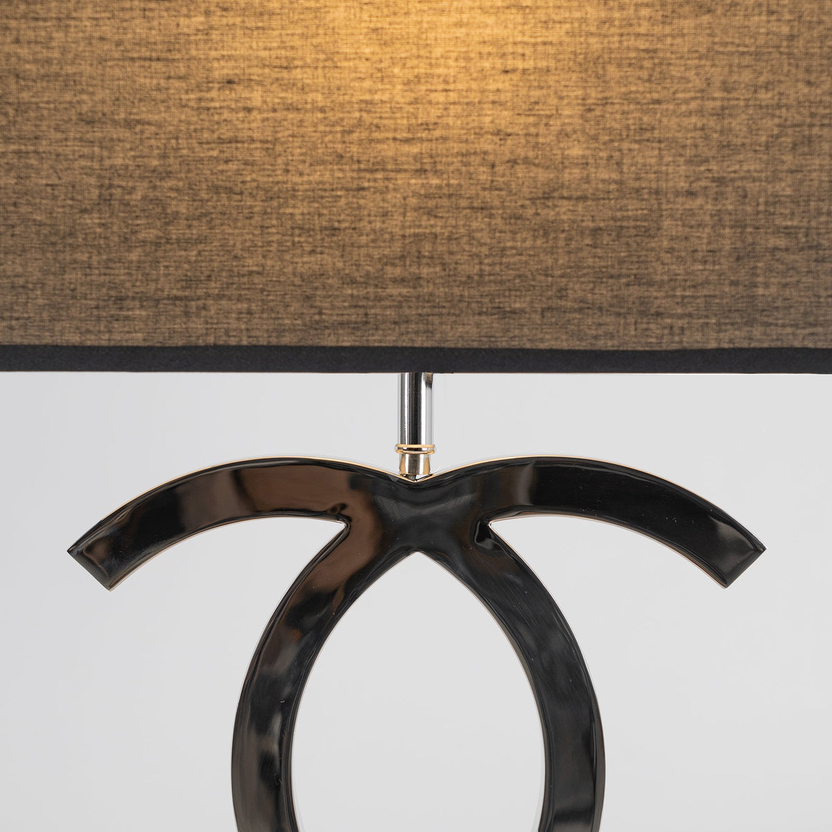 Close view of the textured black fabric shade glowing amber above the dark chrome loops of this Clérachic table lamp.