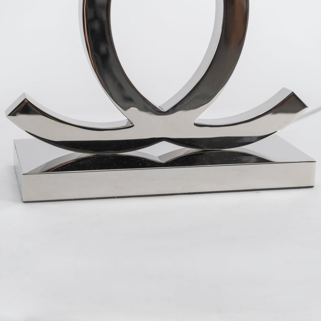 Close view of the lower curve of the loops and the stepped steel base on this Clérachic table lamp, against a pale backdrop.