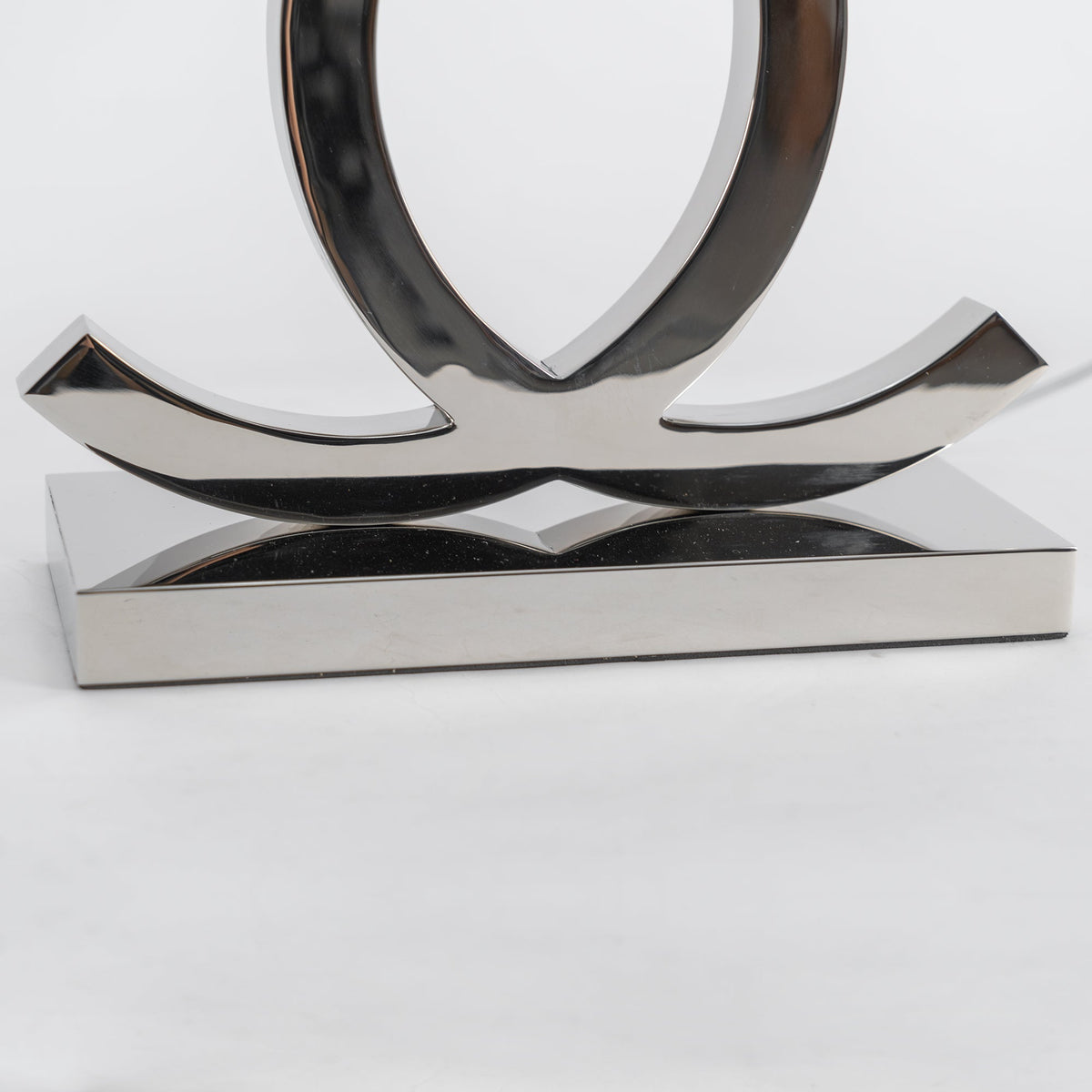 Close view of the lower curve of the loops and the stepped steel base on this Clérachic table lamp, against a pale backdrop.