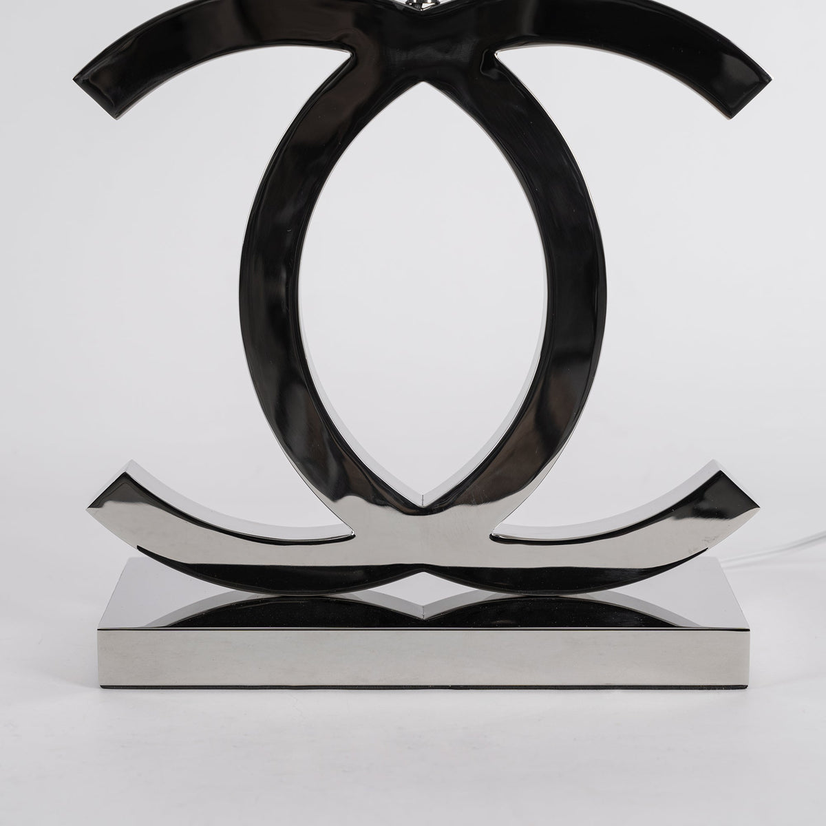 Close view of the polished dark chrome loops and the flat rectangular base of this Clérachic table lamp, against a pale backdrop.