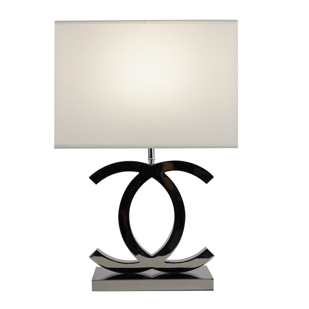 Clérachic table lamp with a lit white shade over dark chrome loops on a polished steel base, on a white backdrop.