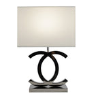 Clérachic table lamp with a lit white shade over dark chrome loops on a polished steel base, on a white backdrop.