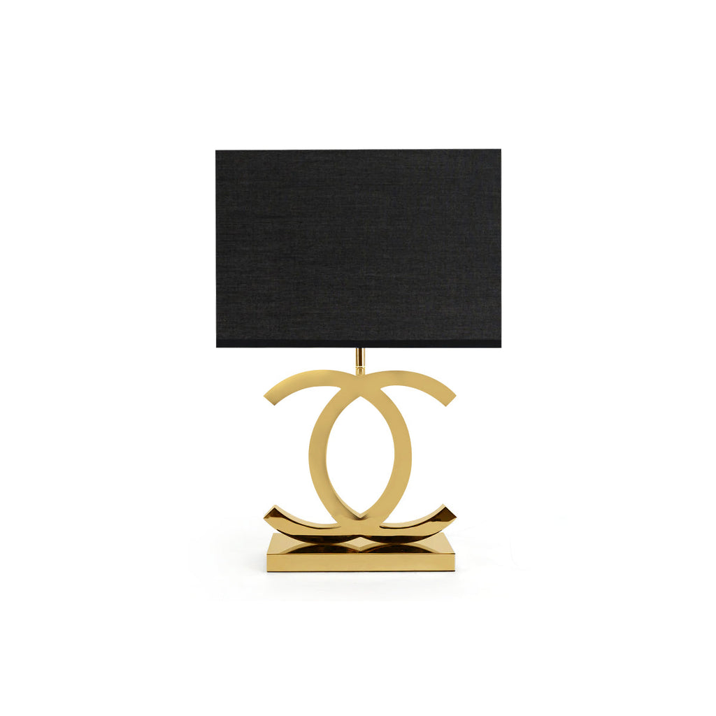 Clérachic gold table lamp with a black rectangular shade, its polished gold loops on a stepped gold base, on a white backdrop.