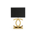 Clérachic gold table lamp with a black rectangular shade, its polished gold loops on a stepped gold base, on a white backdrop.