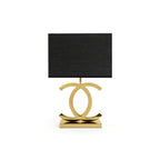 Clérachic gold table lamp with a black rectangular shade, its polished gold loops on a stepped gold base, on a white backdrop.