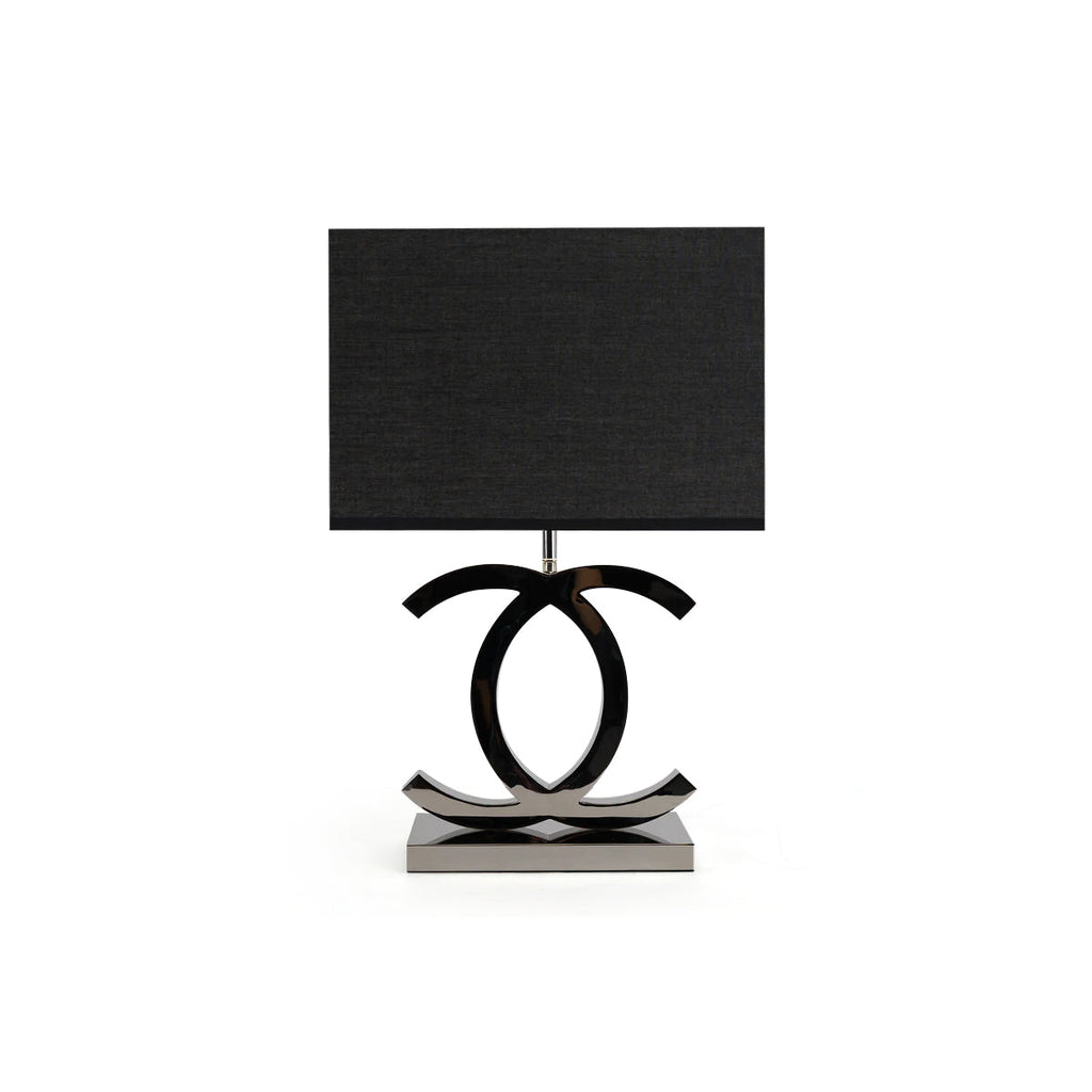 Clérachic table lamp with a black shade, its dark chrome loops standing on a polished steel base, on a white backdrop.