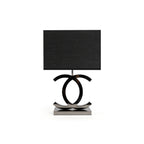 Clérachic table lamp with a black shade, its dark chrome loops standing on a polished steel base, on a white backdrop.