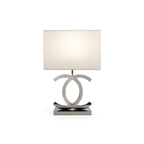 Lit Clérachic table lamp with a white rectangular shade, silver-toned loops and a dark steel base, on a plain white backdrop.