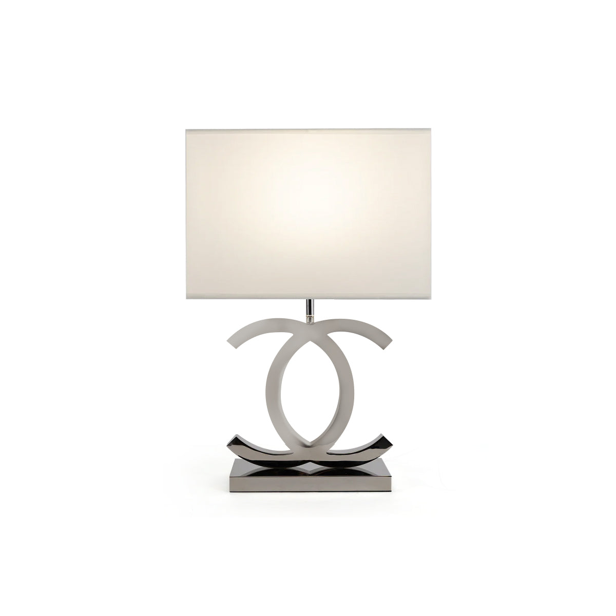 Lit Clérachic table lamp with a white rectangular shade, silver-toned loops and a dark steel base, on a plain white backdrop.