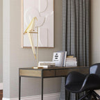 This Clérachic bird lamp on a gold stand sits on a metal desk with books, in front of a relief artwork and houndstooth curtains.