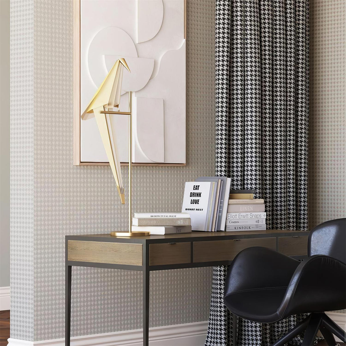 This Clérachic bird lamp on a gold stand sits on a metal desk with books, in front of a relief artwork and houndstooth curtains.