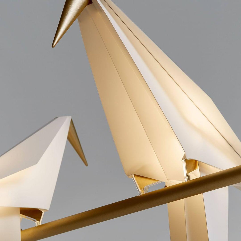 Close view of the folded white paper wings and gold beak of this Clérachic bird lamp, with a second bird blurred in front.