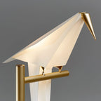 Close view of the folded white bird body and brass-coloured beak of this Clérachic lamp, resting on its gold pivot arm.
