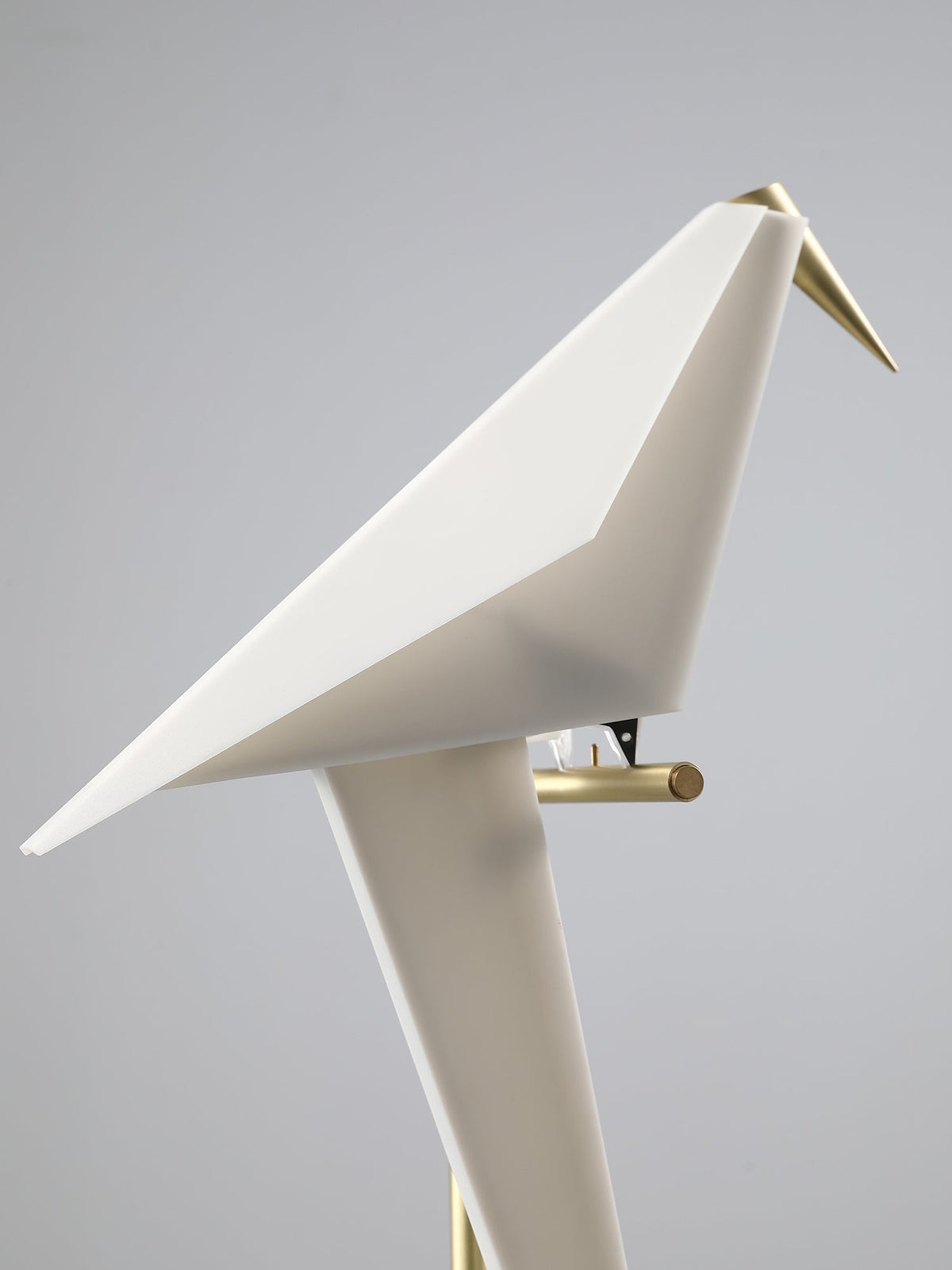 Close view of the unlit white bird of this Clérachic table lamp, its folded planes and gold beak on a pale grey backdrop.