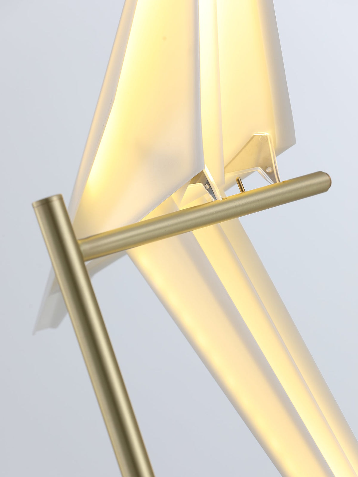 Close view of the gold crossbar the bird of this Clérachic table lamp perches on, with warm light inside its folded body.