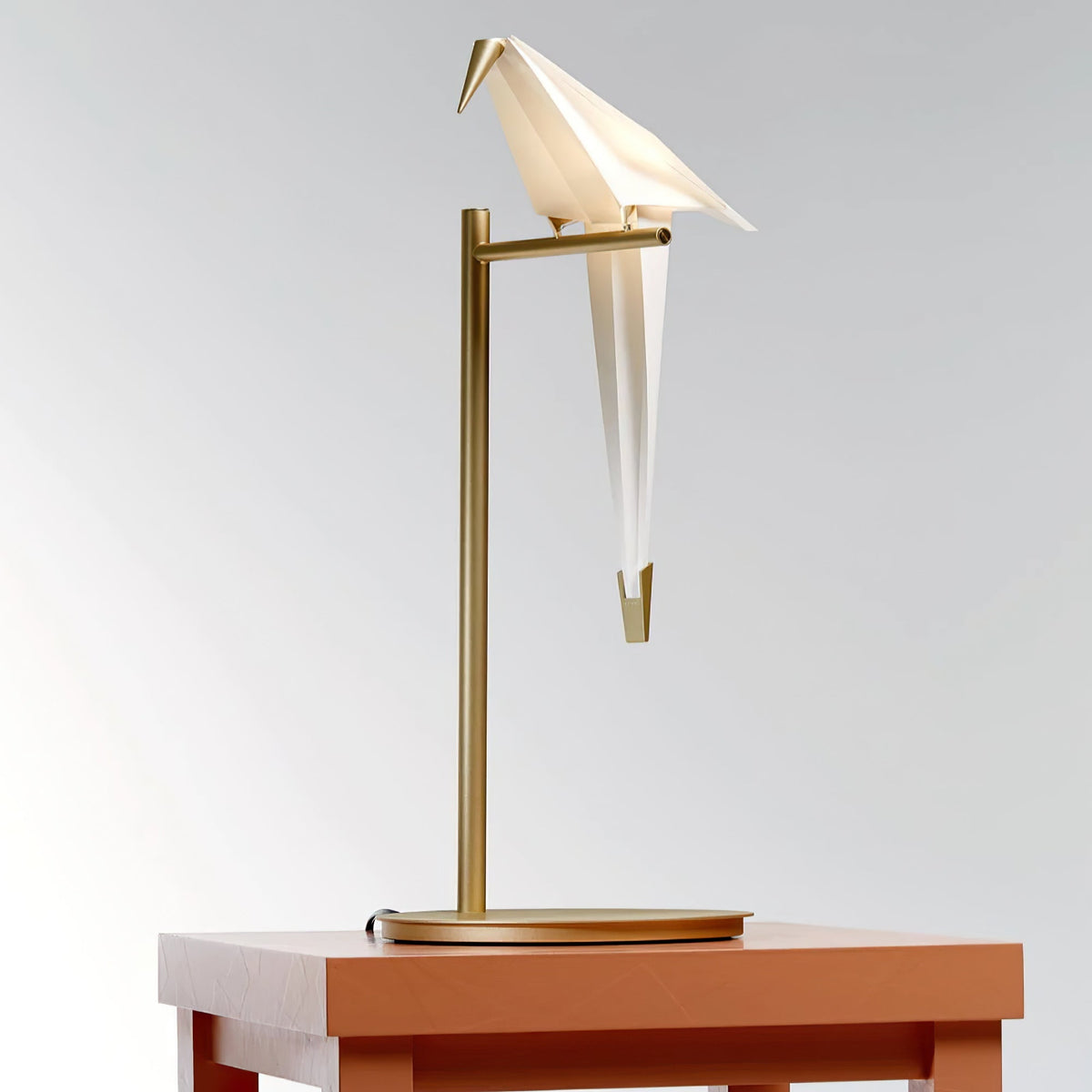 Front view of this Clérachic bird table lamp, its white body hanging below the gold stand, on a terracotta table.