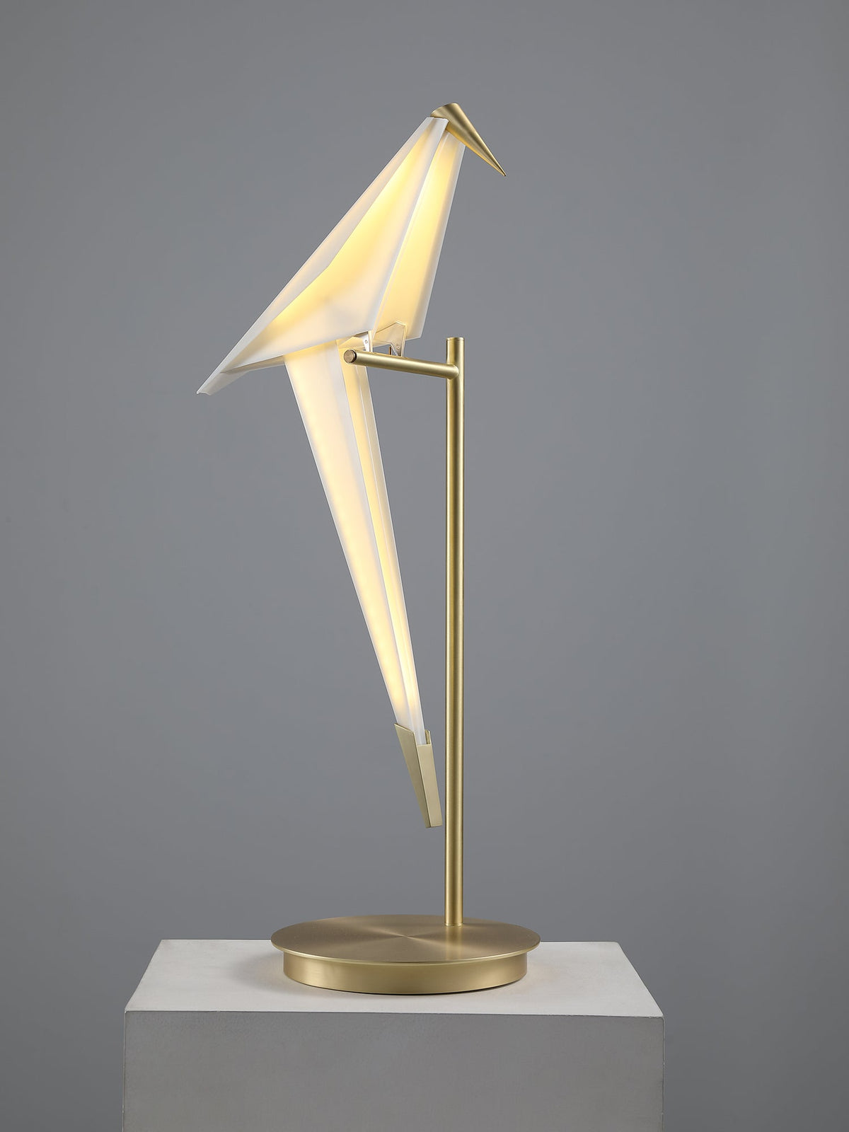 Lit from within, this Clérachic bird table lamp shows its folded white wings and gold tip on a pale plinth.