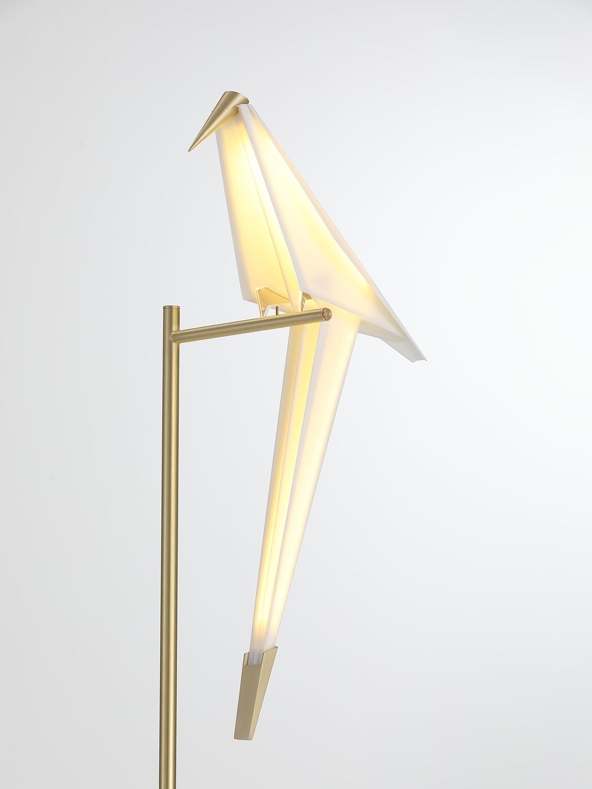 The gold stand and folded white bird of this Clérachic table lamp, lit warm, against a clean white backdrop.