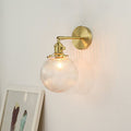 The Clérachic Gold Vanity Wall Sconce lights a pale wall, ribbed globe shade on a gold swivel arm.