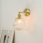 The Clérachic Gold Vanity Wall Sconce lights a pale wall, ribbed globe shade on a gold swivel arm.
