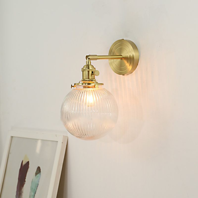 The Clérachic Gold Vanity Wall Sconce lights a pale wall, ribbed globe shade on a gold swivel arm.