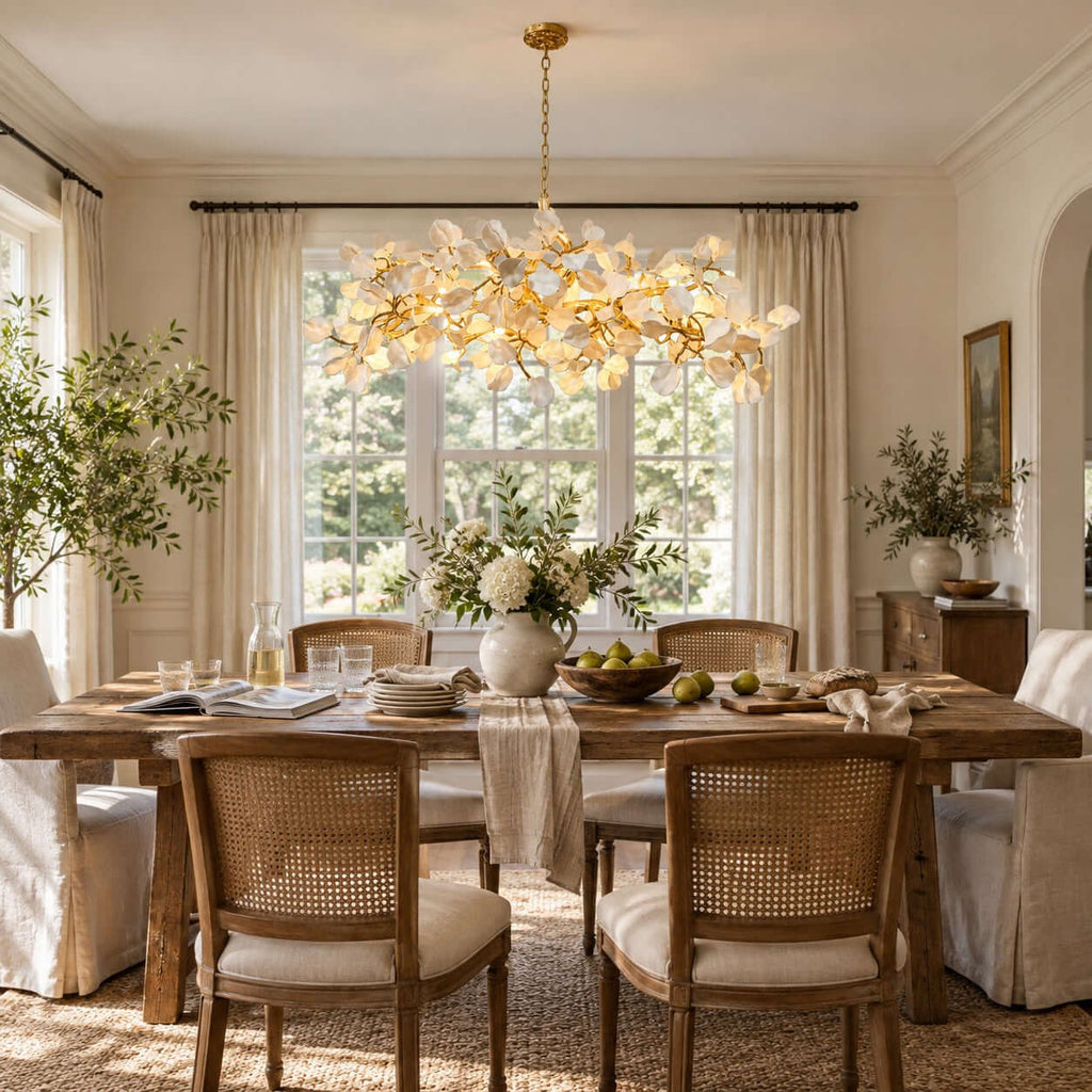 Dining room with this Clérachic petal chandelier hung over a rustic wooden table, cane-back chairs and tall windows with linen curtains.