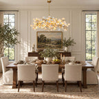 Panelled dining room with a Clérachic chandelier of ceramic petals above a long table set for dinner, with a landscape painting behind.
