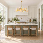White kitchen with a Clérachic vine chandelier above a sage-green island, rattan-seat stools and a marble splashback.