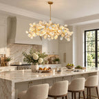 Close view of a Clérachic chandelier's white petals and gold branches, hung above a marble island in a bright kitchen.