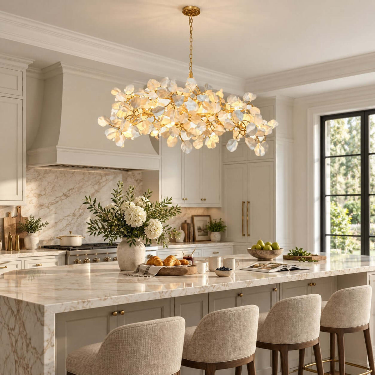 Close view of a Clérachic chandelier's white petals and gold branches, hung above a marble island in a bright kitchen.
