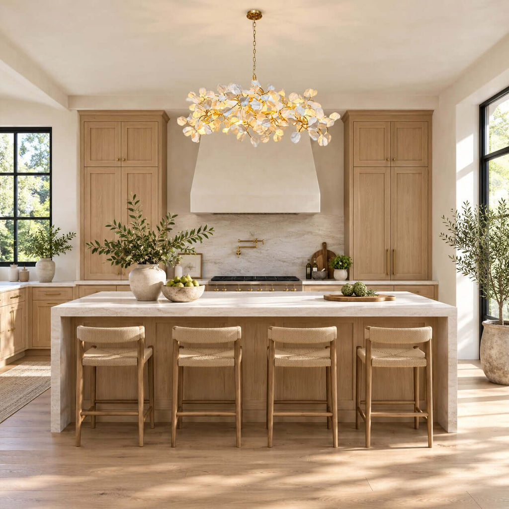 Kitchen in pale oak with a Clérachic chandelier over a long marble-topped island, four woven stools and a plaster range hood.