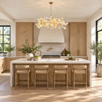 Kitchen in pale oak with a Clérachic chandelier over a long marble-topped island, four woven stools and a plaster range hood.