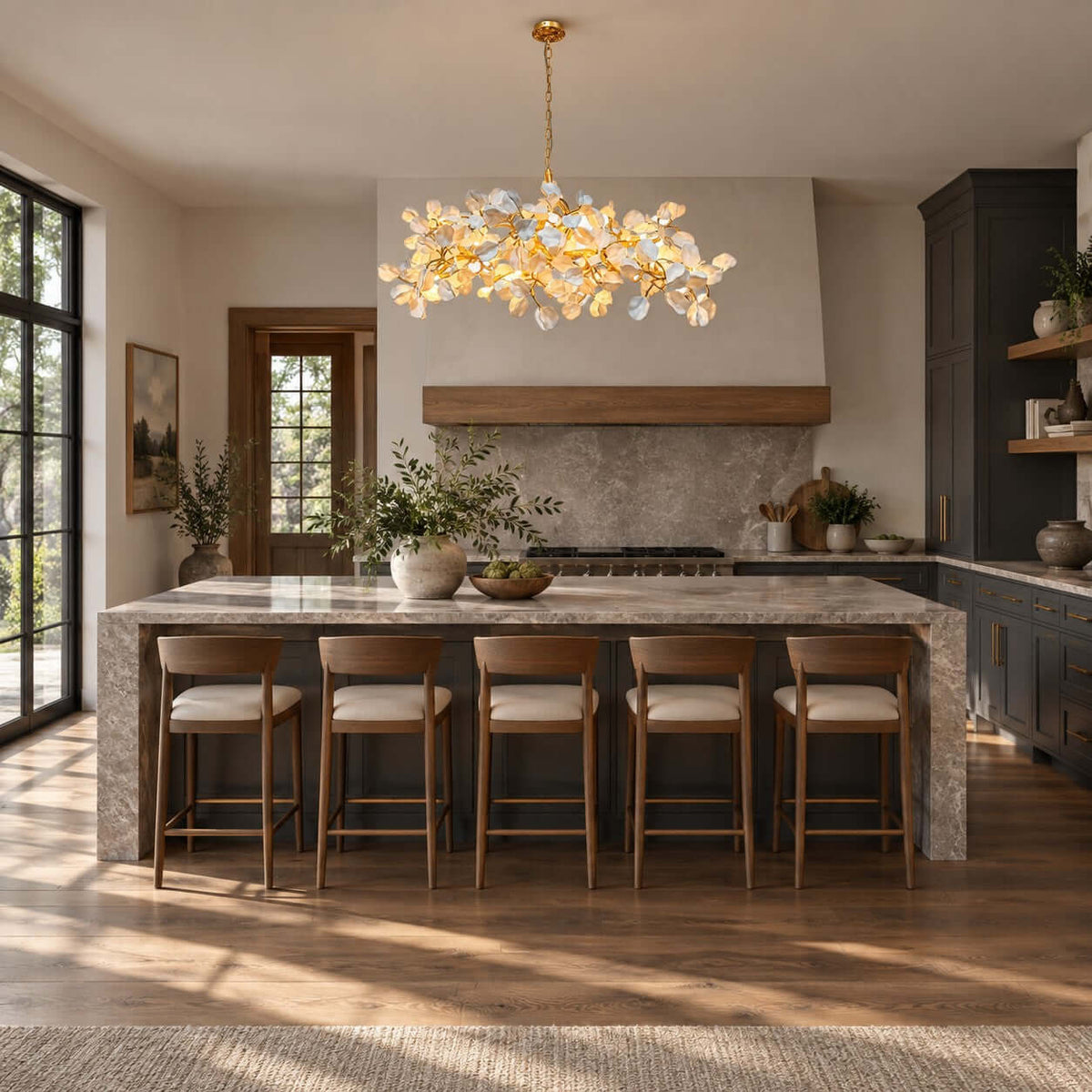 Kitchen with a Clérachic petal chandelier over a stone-topped island and five leather-seat stools, in front of a dark cabinet wall.