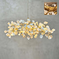 Lit Clérachic chandelier of white ceramic petals on a tangled gold branch frame against a grey plaster wall, with a small detail inset.