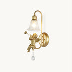 Gold wall light from Clérachic with a cherub blowing a trumpet beneath a clear bell shade, on a plain white backdrop.