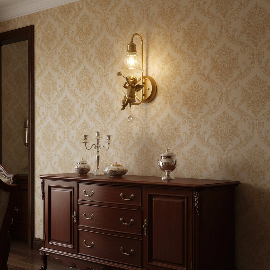 Gold cherub wall light from Clérachic glowing above a dark wood sideboard, against damask wallpaper in cream and gold.