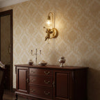 Gold cherub wall light from Clérachic glowing above a dark wood sideboard, against damask wallpaper in cream and gold.