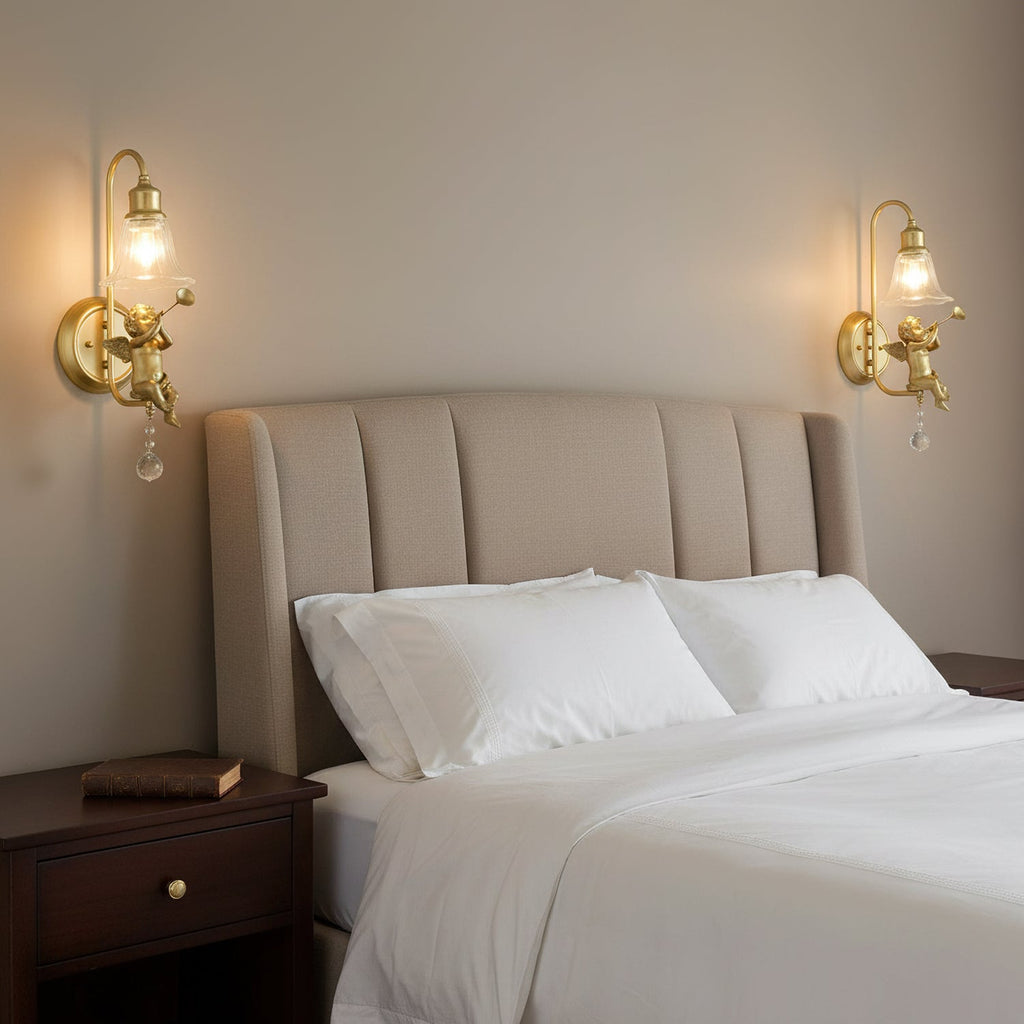 Pair of lit Clérachic gold cherub wall lights either side of a bed with a ribbed upholstered headboard and white linen.
