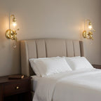 Pair of lit Clérachic gold cherub wall lights either side of a bed with a ribbed upholstered headboard and white linen.