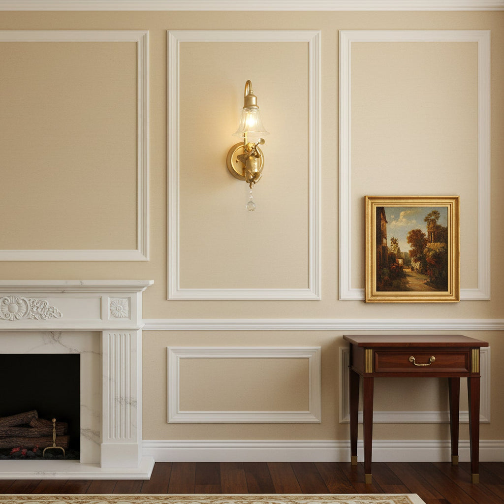 Small Clérachic gold cherub wall light on a cream panelled wall, between a framed landscape and a white fireplace.