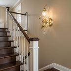 Clérachic wall light with a gold cherub and clear glass shade at a staircase with white balusters and a dark handrail.