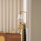 Close view of a gold cherub on a Clérachic wall light, its clear glass bell shade above a wooden chest.