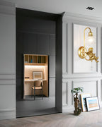 Clérachic gold cherub wall light on a grey panelled wall beside a dark doorway leading to a small desk alcove.