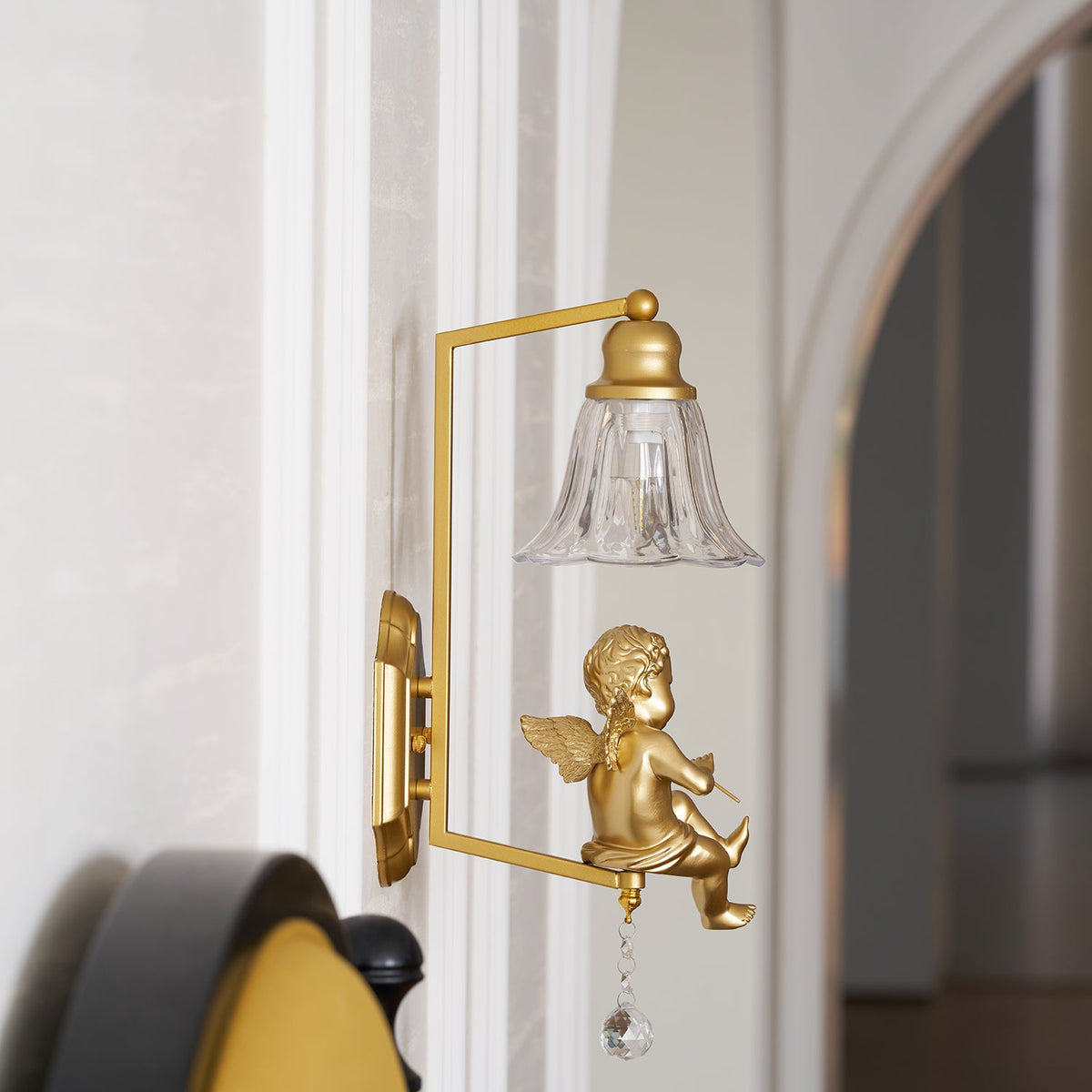 Gold cherub wall light from Clérachic with a square arm and clear glass bell shade, set beside an arched doorway.