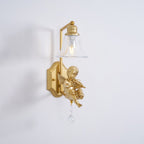 Clérachic gold cherub wall light with a clear bell shade and crystal drop on a pale grey wall, the cherub playing a violin.