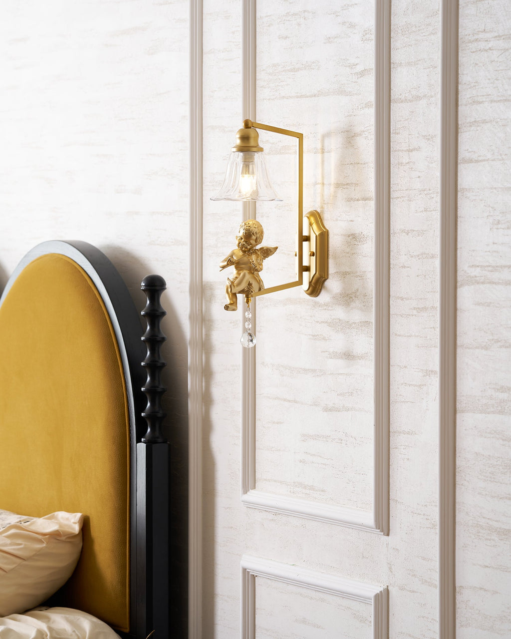 Small Clérachic gold cherub wall light high on a panelled wall, with a mustard headboard and cream bedding below.